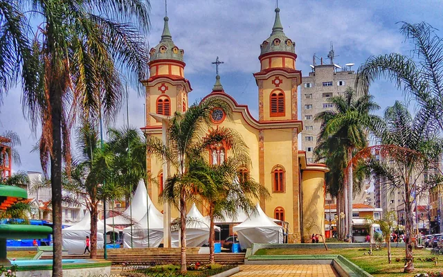 Igreja com árvores e construção ao fundo em Alfenas